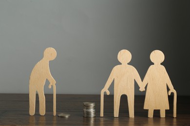 Photo of Financial inequality. Figures of senior man and couple with different amount of coins on wooden table