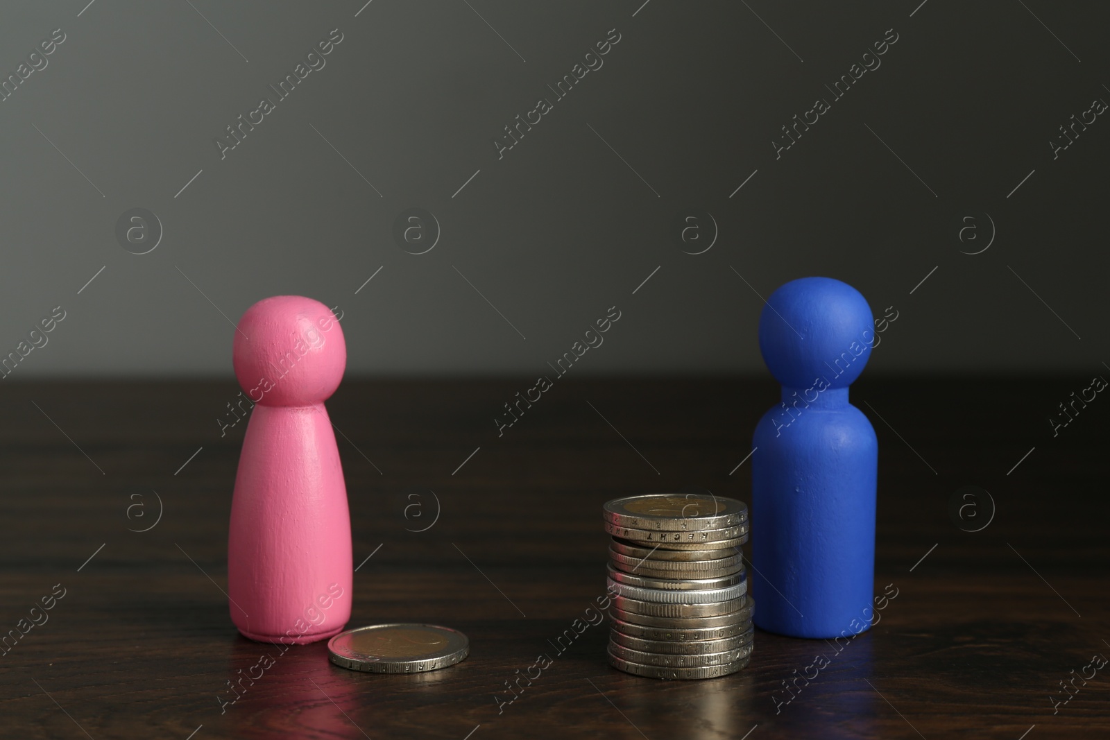 Photo of Financial inequality. Male and female figures with uneven amount of coins on wooden table