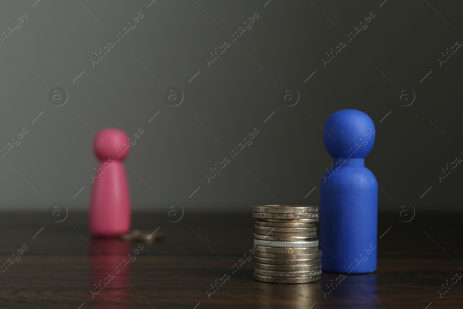 Photo of Financial inequality. Male and female figures with uneven amount of coins on wooden table