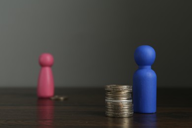 Photo of Financial inequality. Male and female figures with uneven amount of coins on wooden table