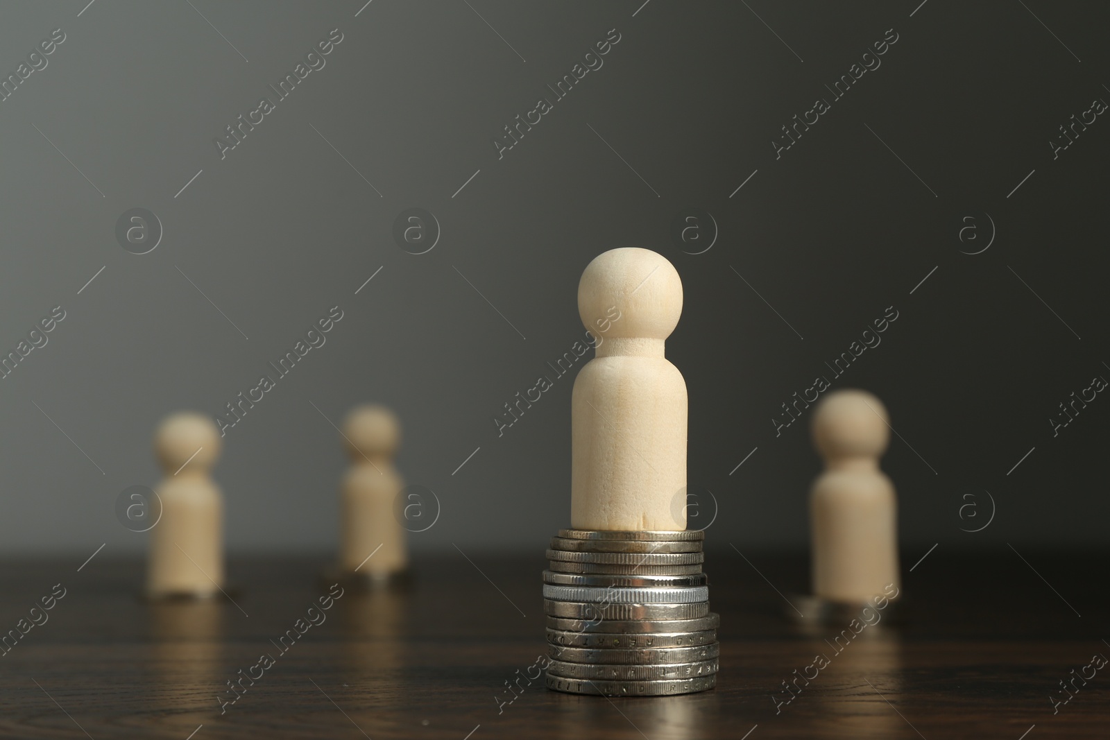 Photo of Financial inequality. One wooden figure with bigger stack of coins than others on table