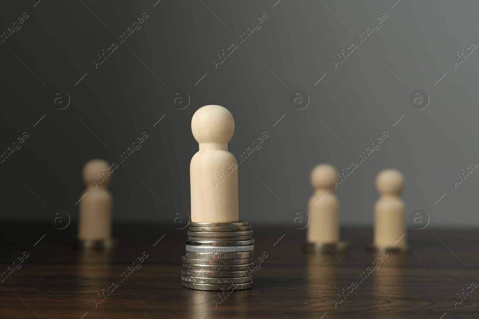 Photo of Financial inequality. One wooden figure with bigger stack of coins than others on table