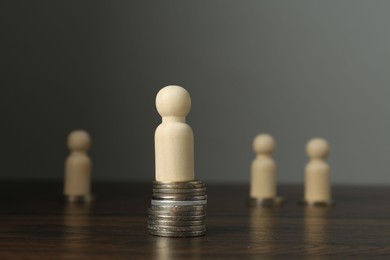 Financial inequality. One wooden figure with bigger stack of coins than others on table