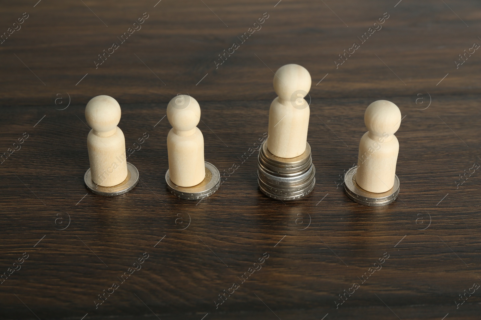 Photo of Financial inequality. One wooden figure with bigger stack of coins than others on table