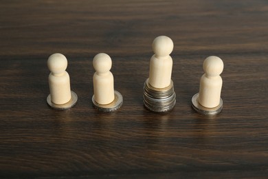 Financial inequality. One wooden figure with bigger stack of coins than others on table