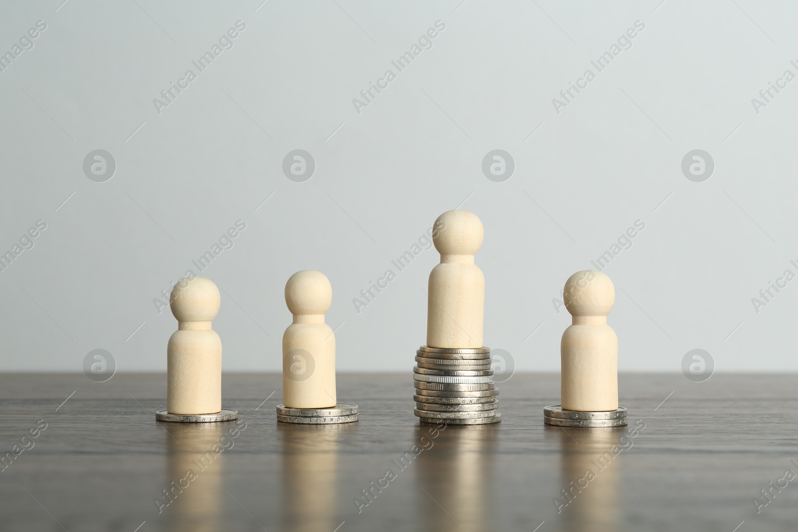 Photo of Financial inequality. One wooden figure with bigger stack of coins than others on table