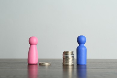 Photo of Financial inequality. Male and female figures with uneven amount of coins on wooden table