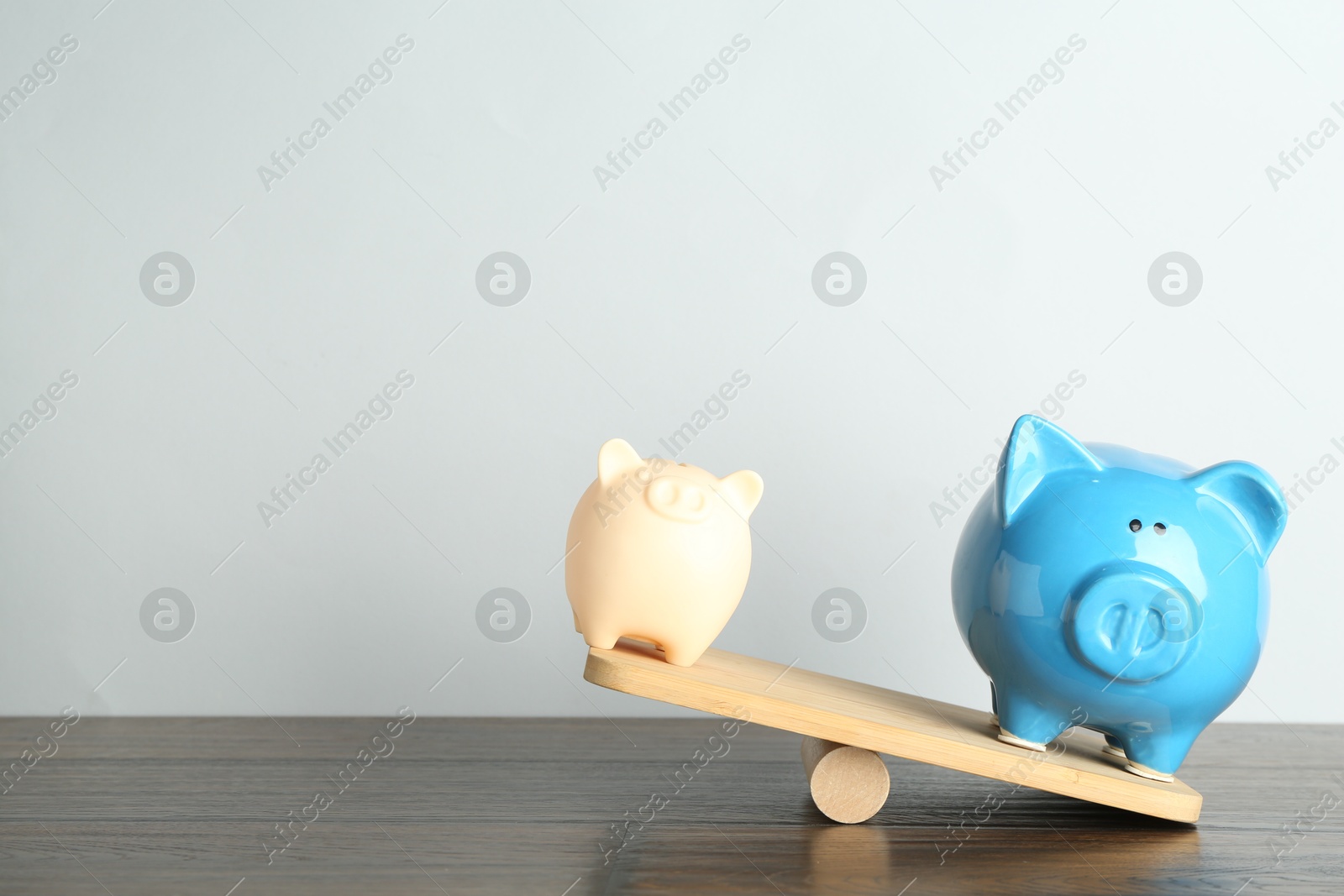 Photo of Financial inequality. Bigger piggy bank overweighting smaller one on scales on wooden table. Space for text