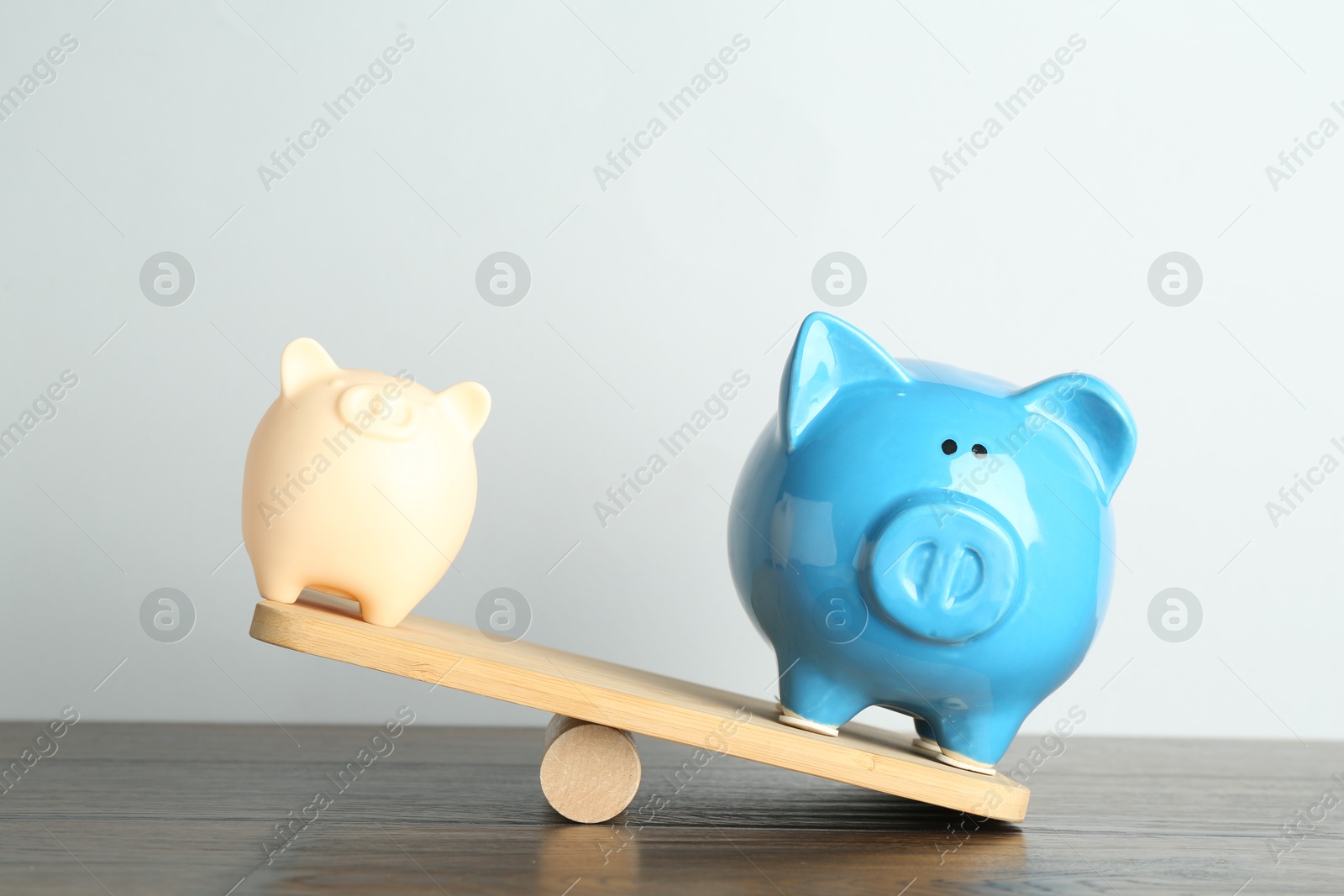 Photo of Financial inequality. Bigger piggy bank overweighting smaller one on scales on wooden table