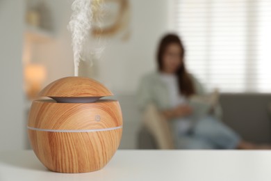 Essential oil diffuser on table, space for text. Woman reading book in room, selective focus