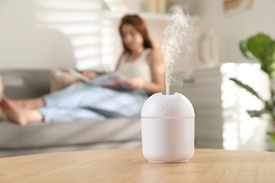 Image of Essential oil diffuser on table, space for text. Woman reading book in room, selective focus