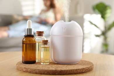 Aroma diffuser and bottles of essential oils on table. Woman reading book in room, selective focus