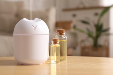 Image of Aroma diffuser and bottles of essential oil on table in room, space for text