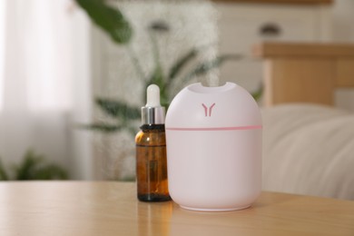 Aroma diffuser and bottle of essential oil on table in room