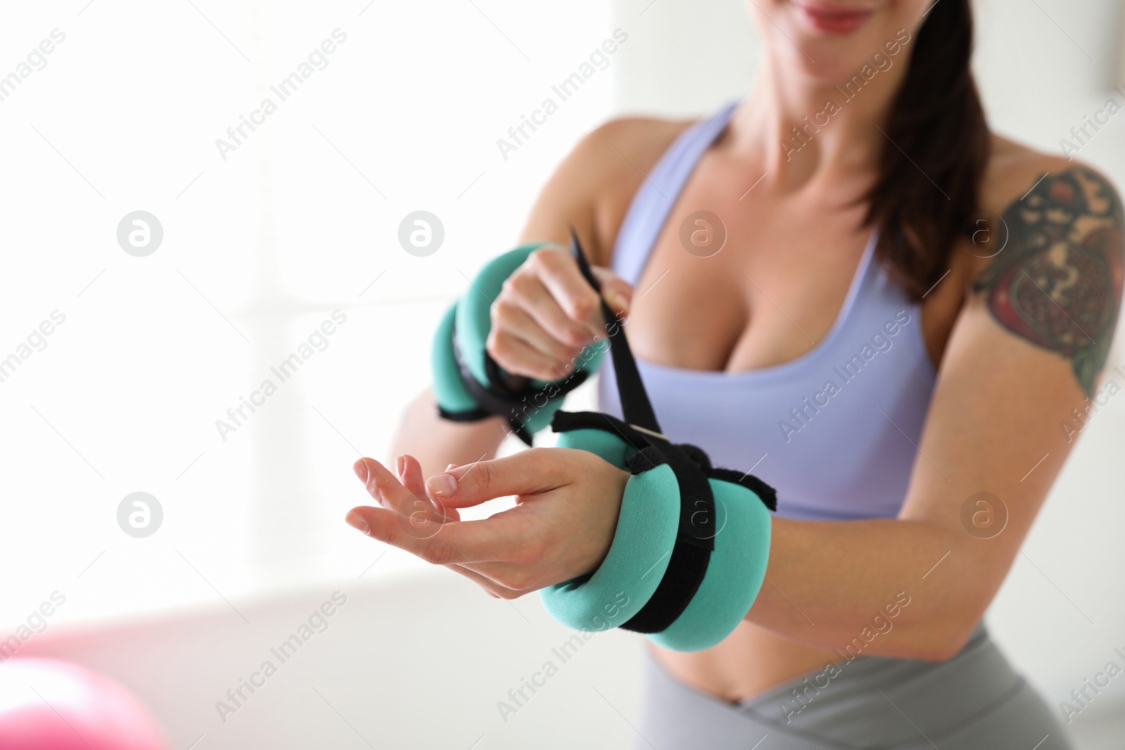 Photo of Woman putting ankle weight on her arm indoors, closeup