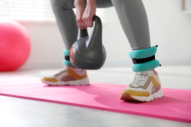 Photo of Woman with ankle weights and kettlebell training indoors, closeup