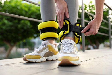 Photo of Woman putting on ankle weights outdoors, closeup