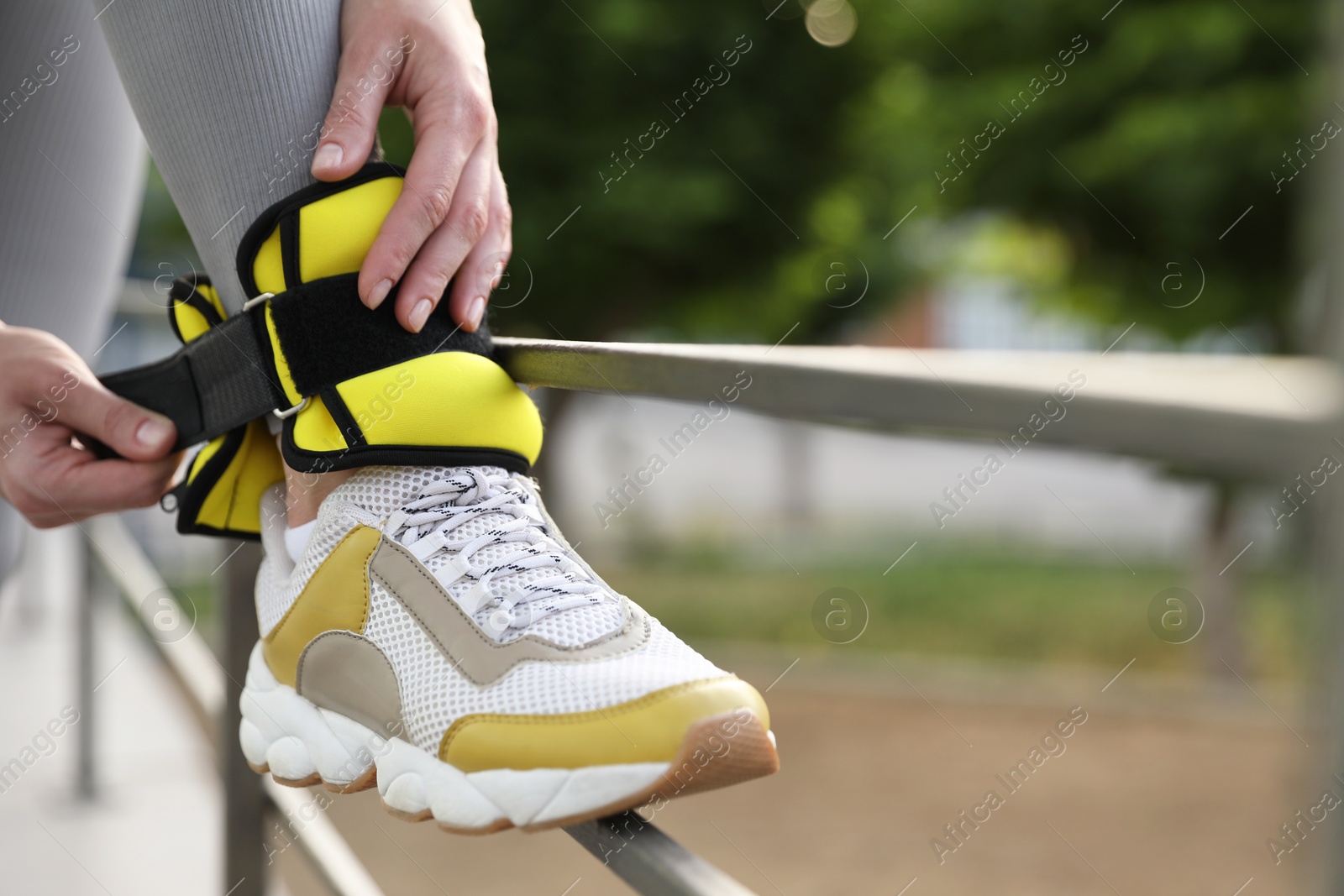 Photo of Woman putting on ankle weights outdoors, closeup