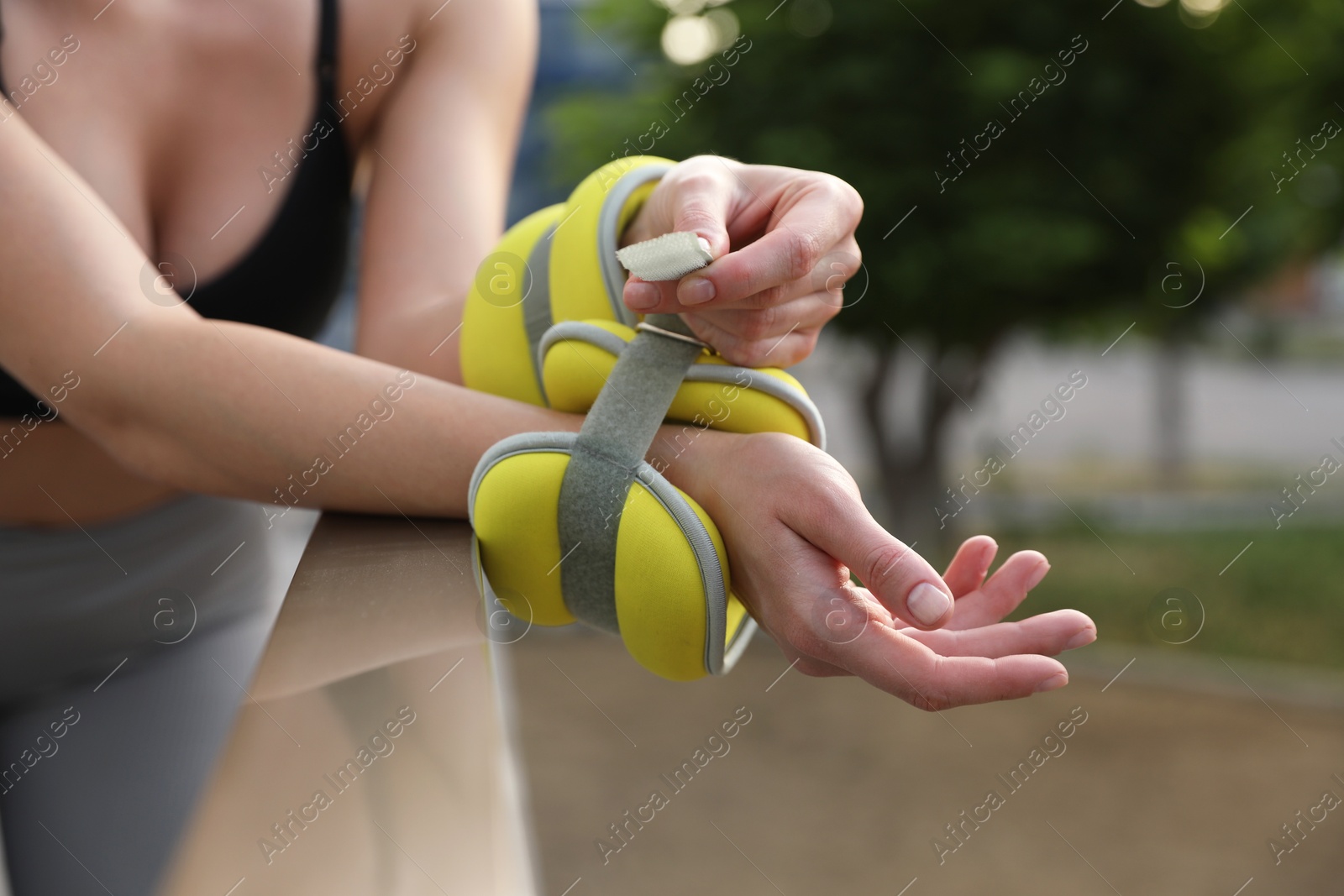 Photo of Woman putting ankle weight on her arm outdoors, closeup