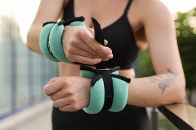 Woman putting ankle weight on her arm outdoors, closeup