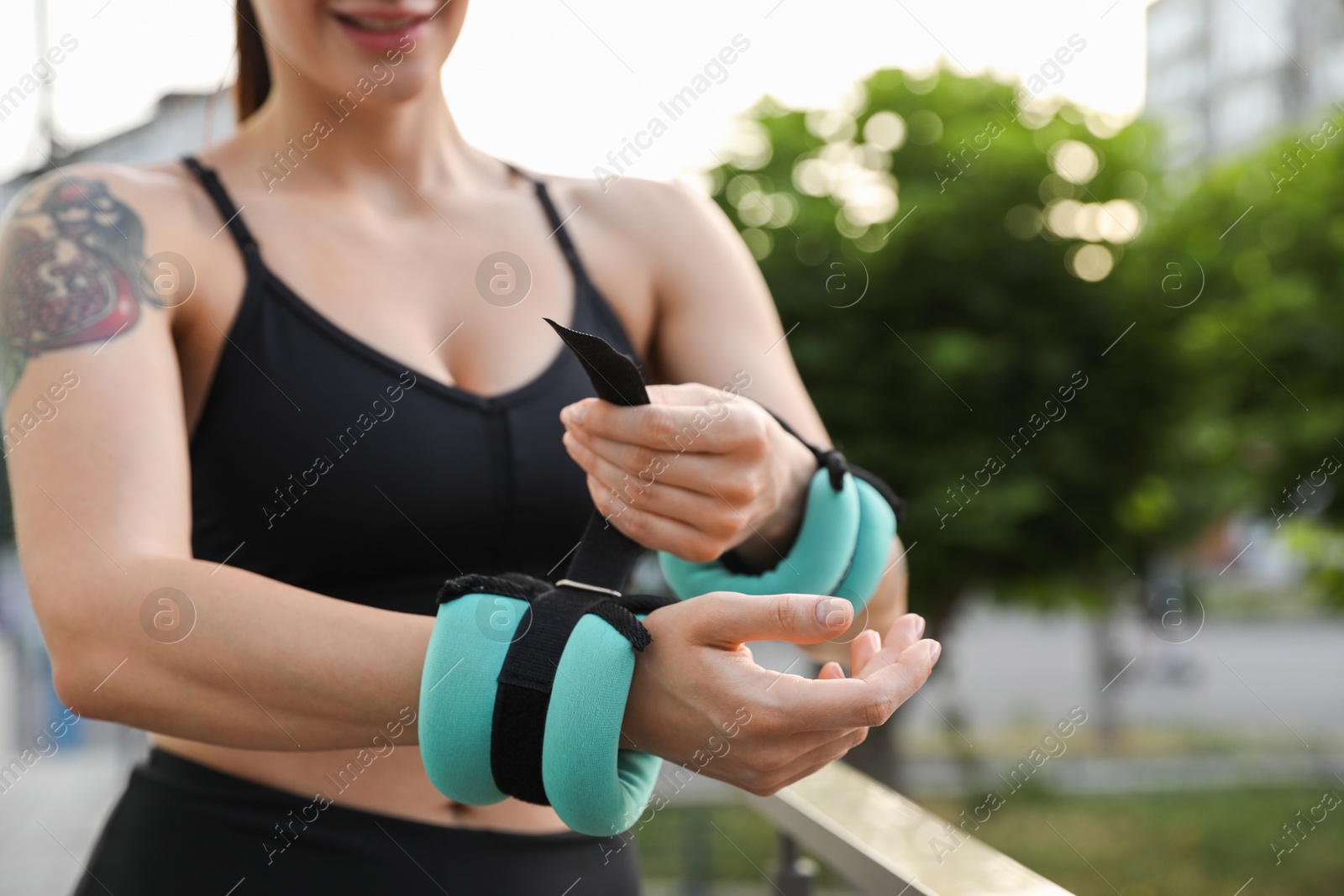 Photo of Woman putting ankle weight on her arm outdoors, closeup