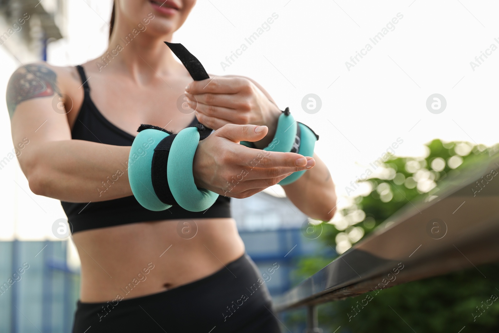 Photo of Woman putting ankle weight on her arm outdoors, closeup