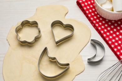 Raw dough and cookie cutters on white wooden table, above view