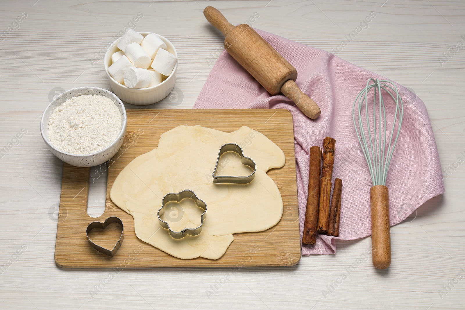 Photo of Raw dough, cookie cutters, rolling pin, whisk and flour on white wooden table, above view