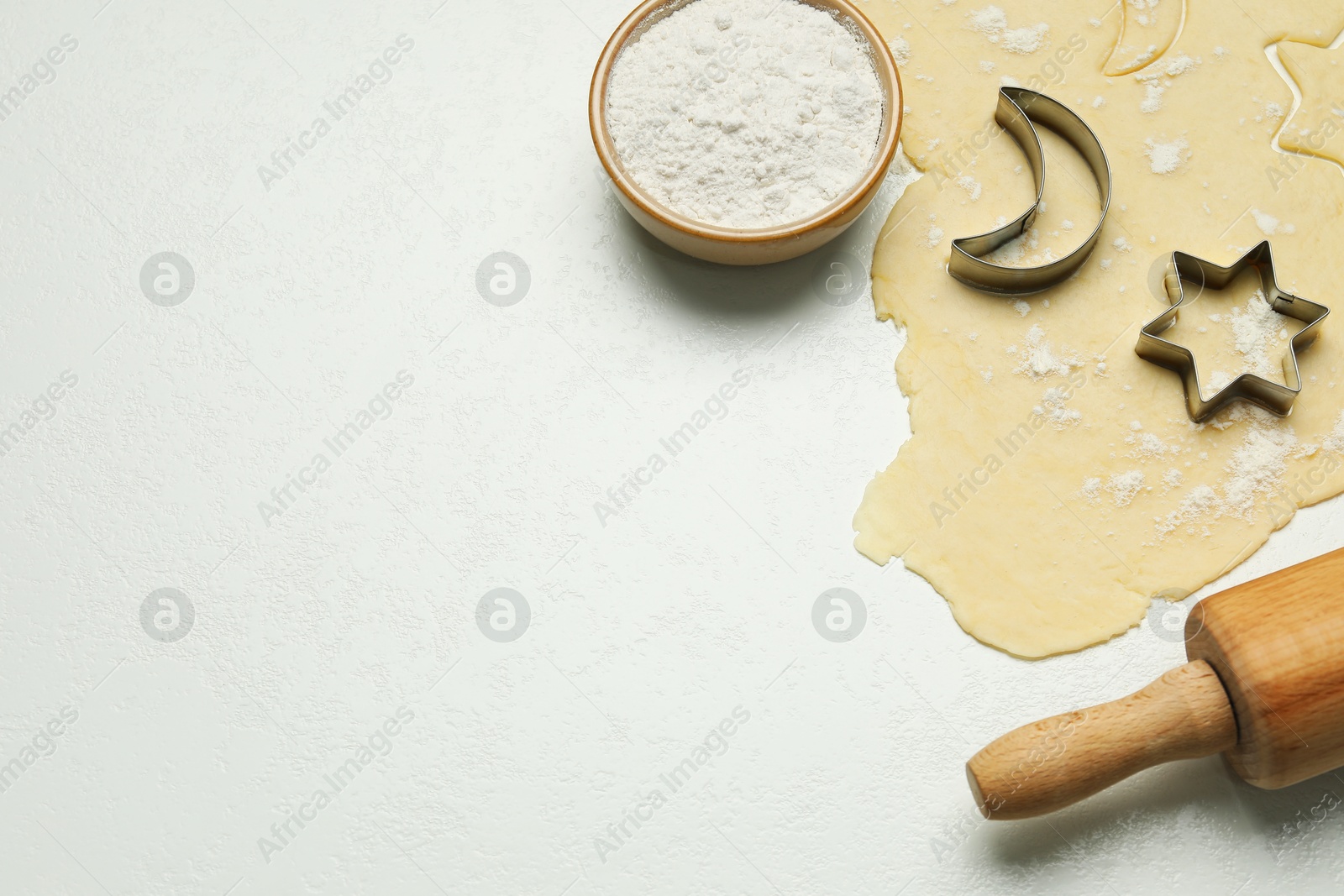 Photo of Raw dough, cookie cutters and rolling pin on white table, above view. Space for text