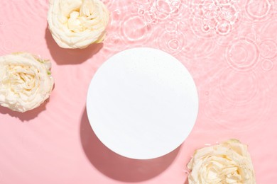 Photo of Beautiful rose flowers and round shaped podium in water on pink background, flat lay