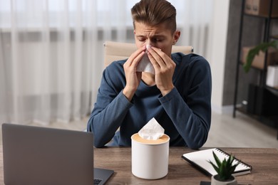 Photo of Young man with tissue suffering from sinusitis at wooden table indoors