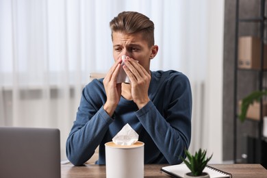 Young man with tissue suffering from sinusitis at wooden table indoors