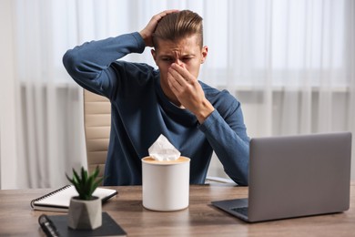 Photo of Young man with tissue suffering from sinusitis at wooden table indoors