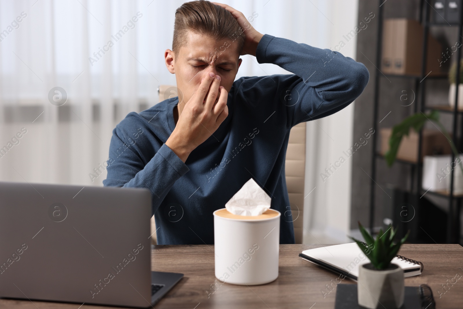 Photo of Young man with tissue suffering from sinusitis at wooden table indoors