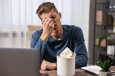 Young man with tissue suffering from sinusitis at wooden table indoors