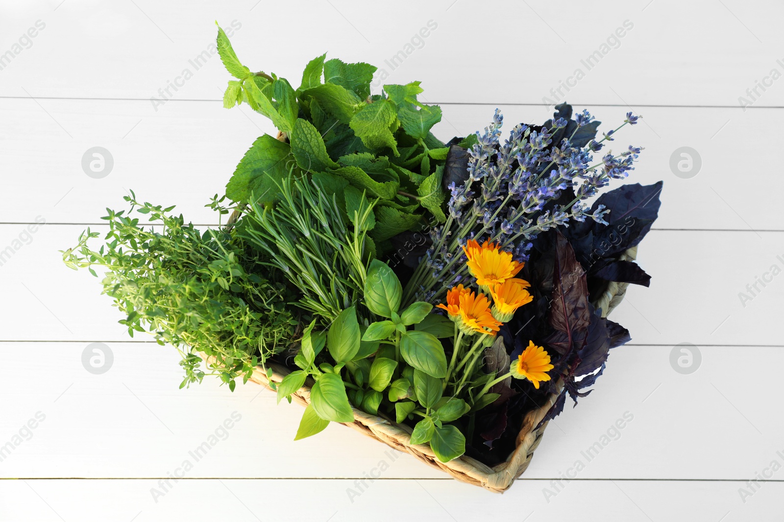 Photo of Different aromatic herbs in basket on white wooden table, top view