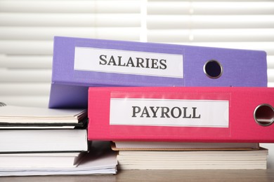 Photo of Office folders with words Payroll and Salaries on wooden table, closeup