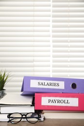 Office folders with words Payroll and Salaries, glasses and stationery on wooden table. Space for text