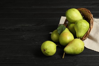 Photo of Fresh green pears and wicker basket on black wooden table. Space for text