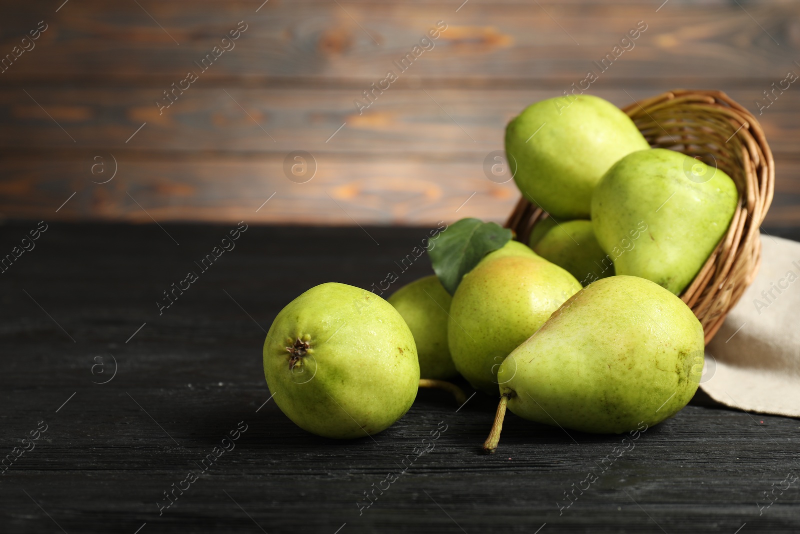 Photo of Fresh green pears and wicker basket on black wooden table. Space for text