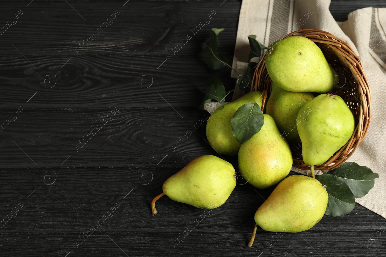 Photo of Fresh green pears and wicker basket on black wooden table, flat lay. Space for text