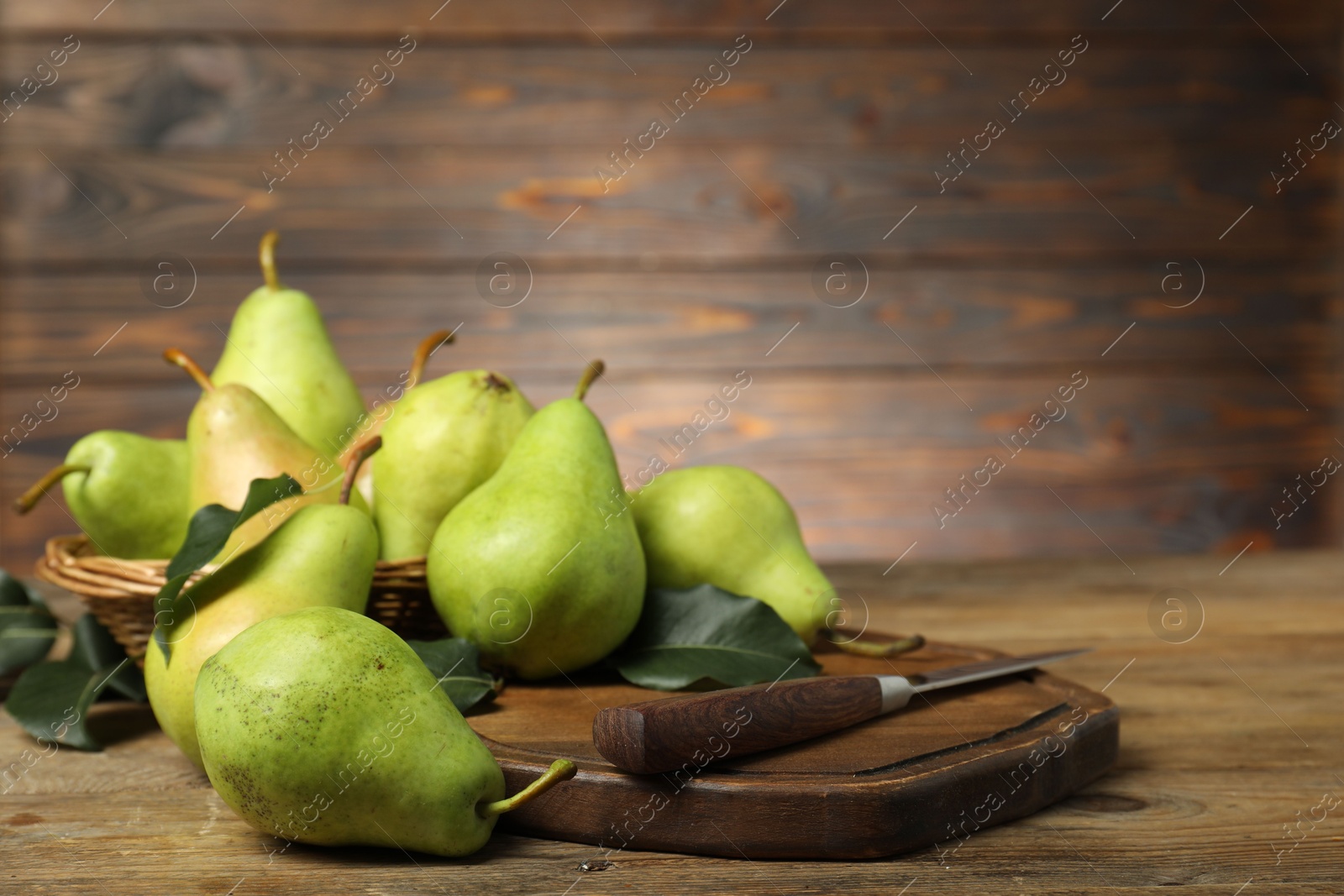 Photo of Fresh green pears, leaves and knife on wooden table, closeup. Space for text