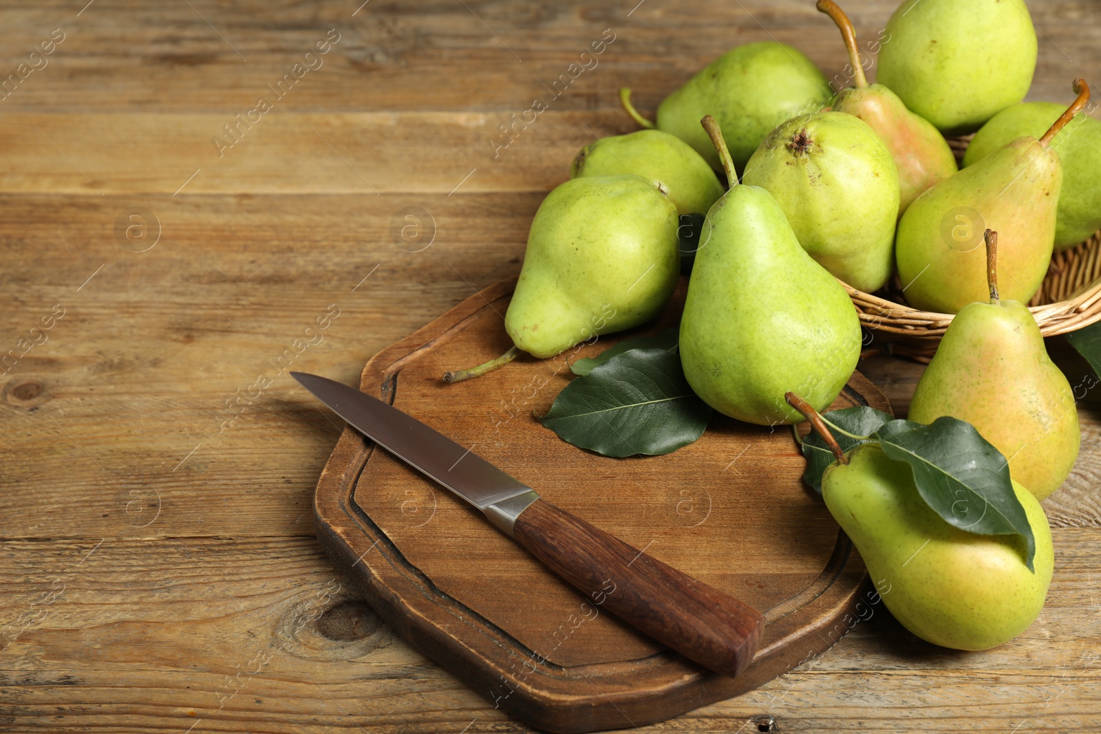 Photo of Fresh green pears, leaves and knife on wooden table. Space for text