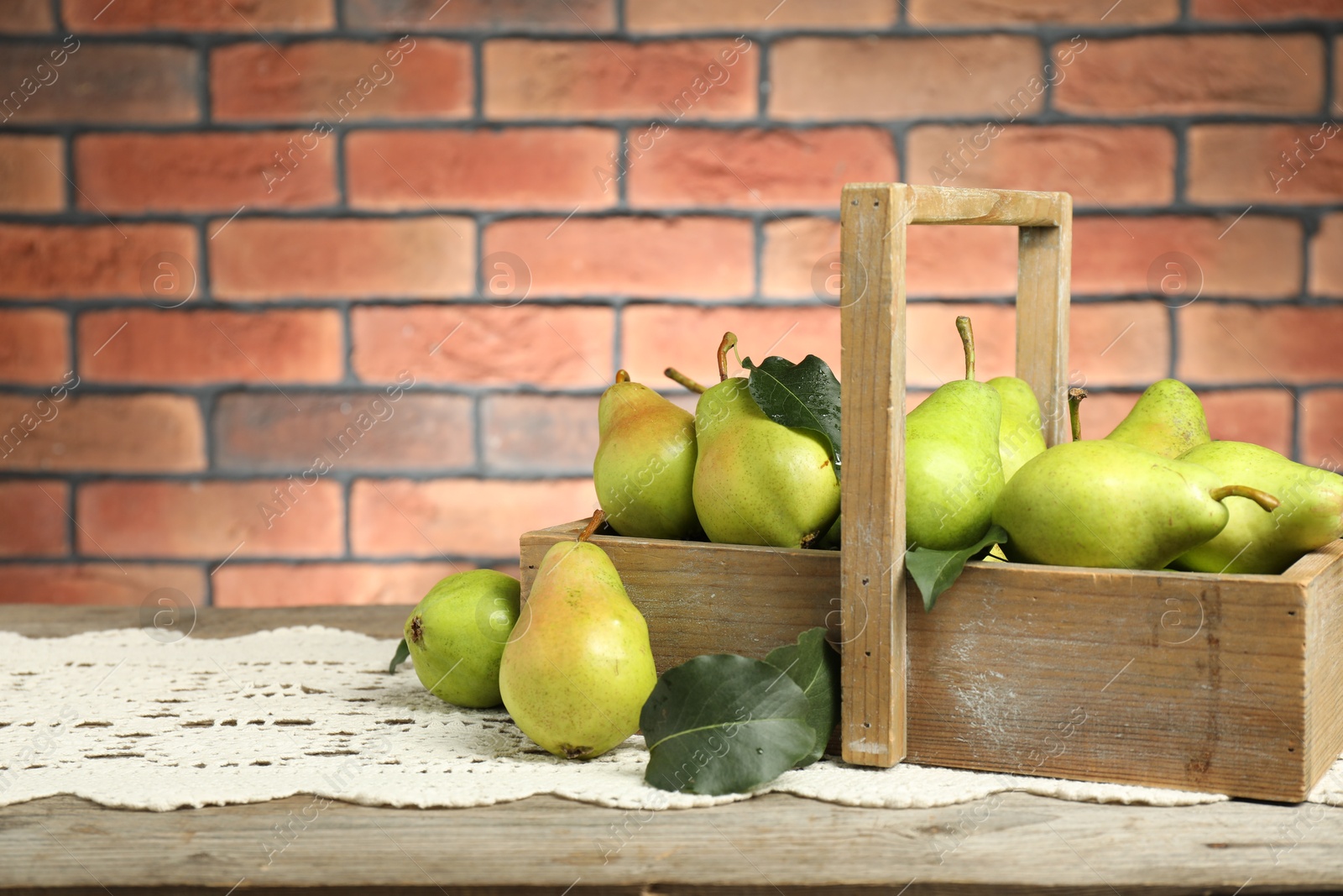 Photo of Crate with fresh green pears and leaves on wooden table against brick wall. Space for text