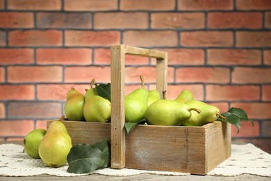 Photo of Crate with fresh green pears and leaves on wooden table against brick wall, closeup