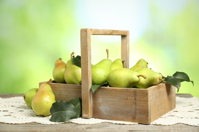 Photo of Crate with fresh pears and leaves on wooden table against blurred green background, closeup