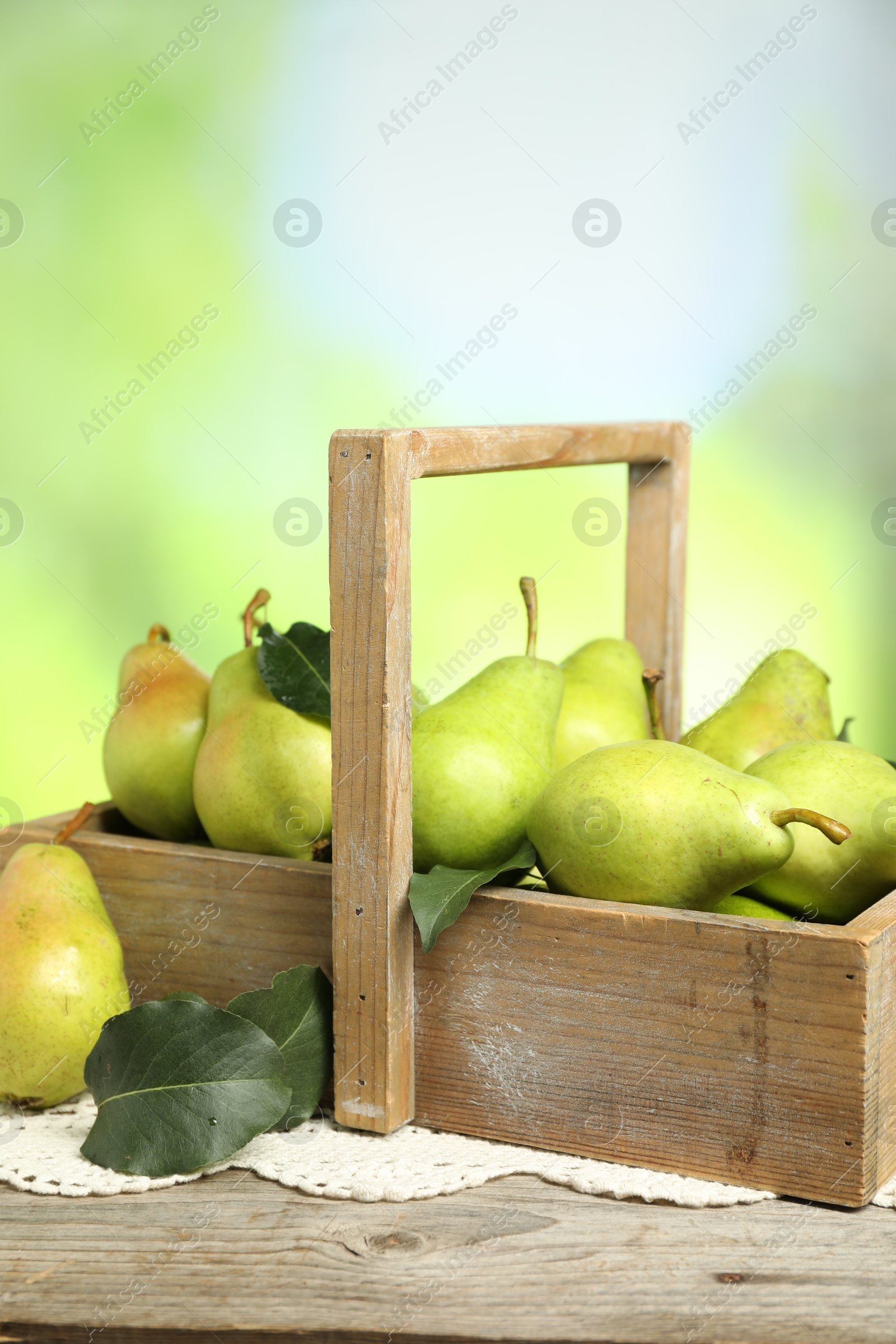 Photo of Crate with fresh pears and leaves on wooden table against blurred green background