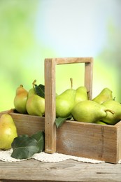 Photo of Crate with fresh pears and leaves on wooden table against blurred green background