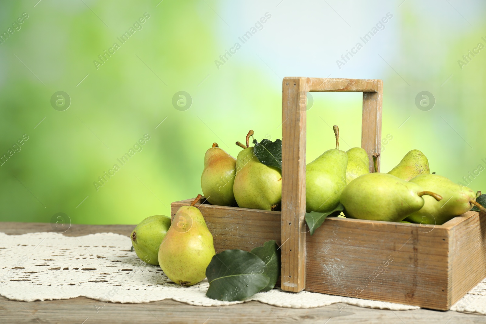 Photo of Crate with fresh pears and leaves on wooden table against blurred green background. Space for text