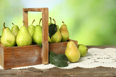 Photo of Crate with fresh pears and leaves on wooden table against blurred green background, closeup. Space for text